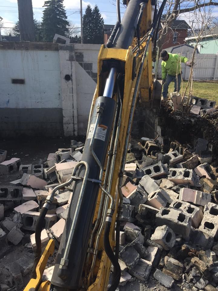 Construction worker using excavator to demolish brick wall. Debris is scattered around the work site.