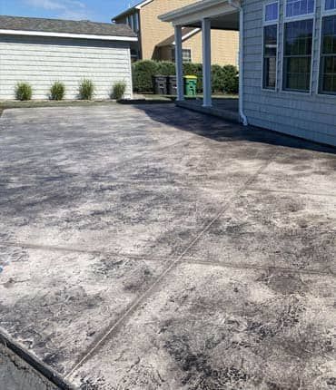 Concrete patio with mottled gray and white pattern; part of a house and small shed visible in the background.