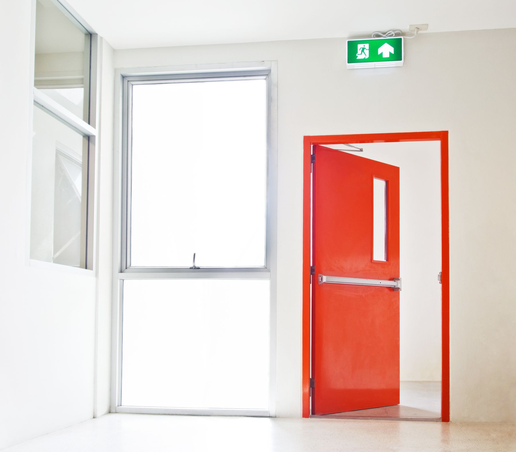 An empty hallway with a red door and a green exit sign