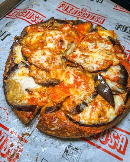 Pizza con melanzane e formaggio fuso, tagliata a fette, su un foglio con scritto "FUKUCCIOSA".