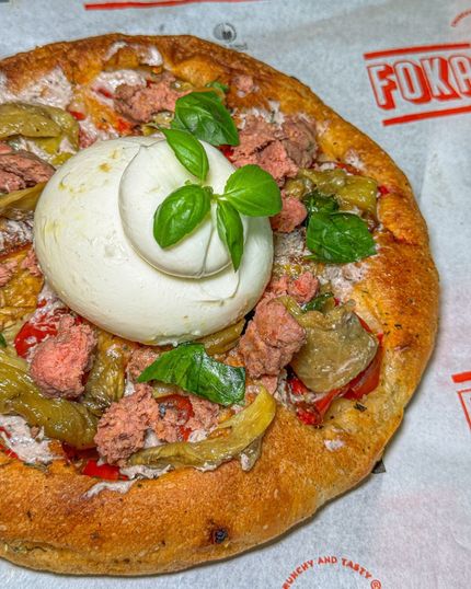 Pizza rotonda condita con una grande palla di formaggio cremoso, rametti di basilico, verdure e carne.