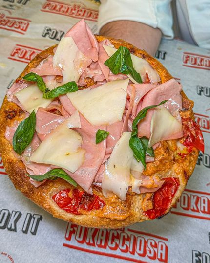 Focaccia con mortadella, parmigiano e basilico. Il sugo rosso e i pomodori bruciacchiati sono visibili sul pane.