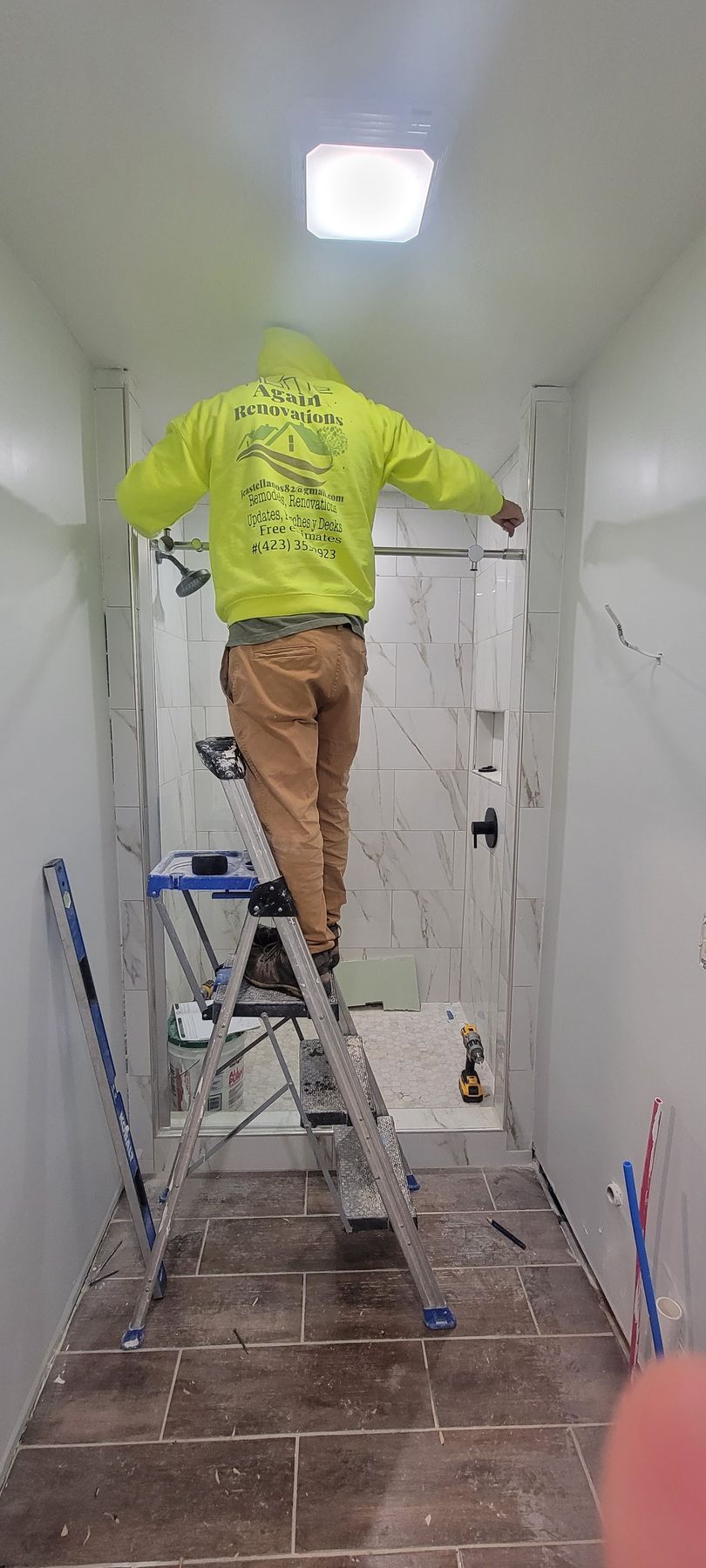 A man is standing on a ladder in a bathroom.