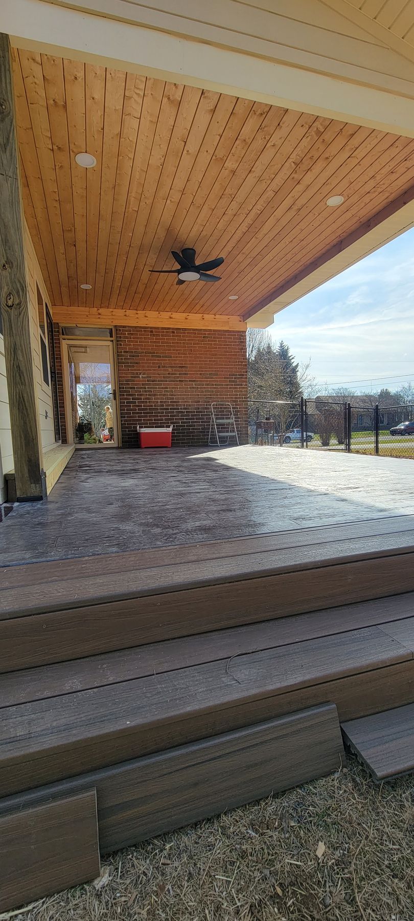 A wooden porch with a ceiling fan and steps leading to it.