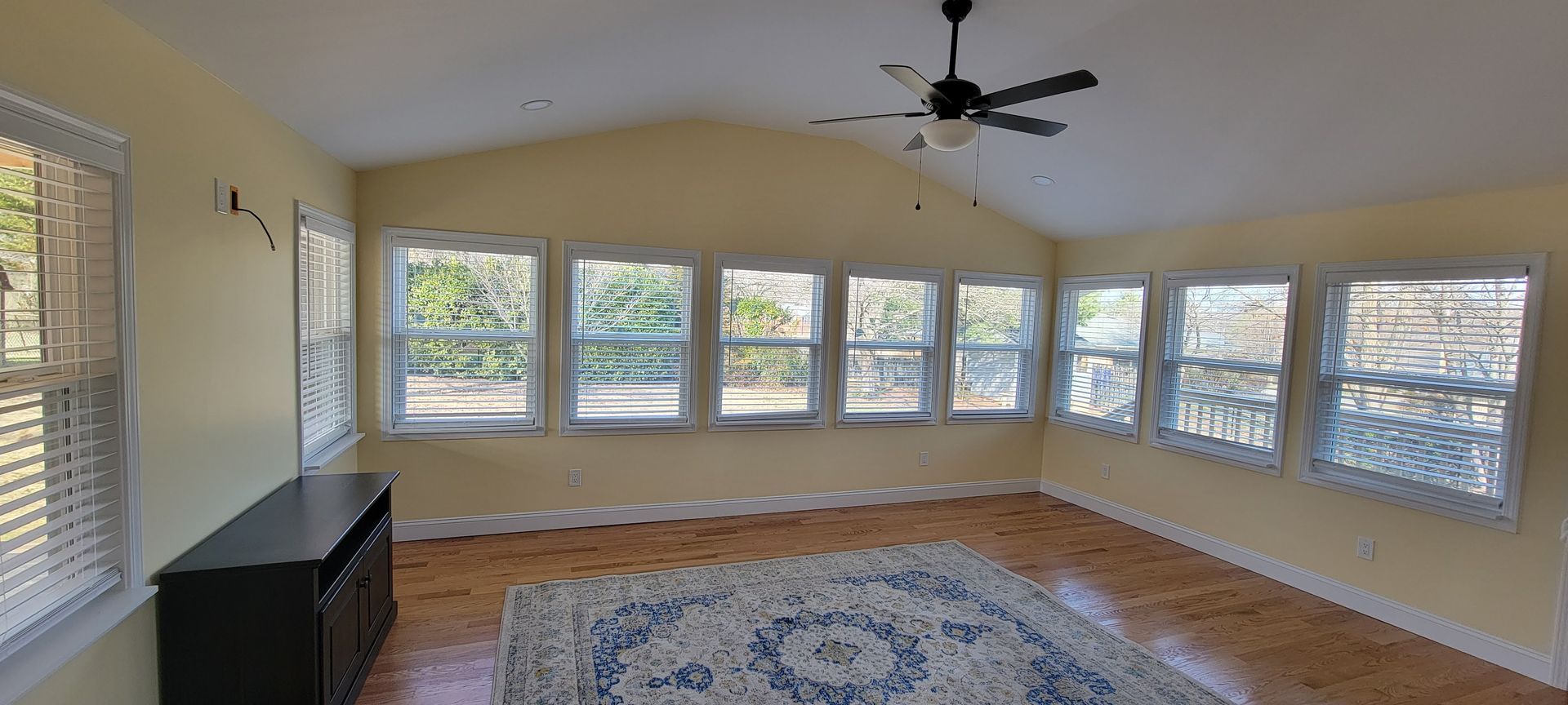 A living room with a lot of windows and a ceiling fan.