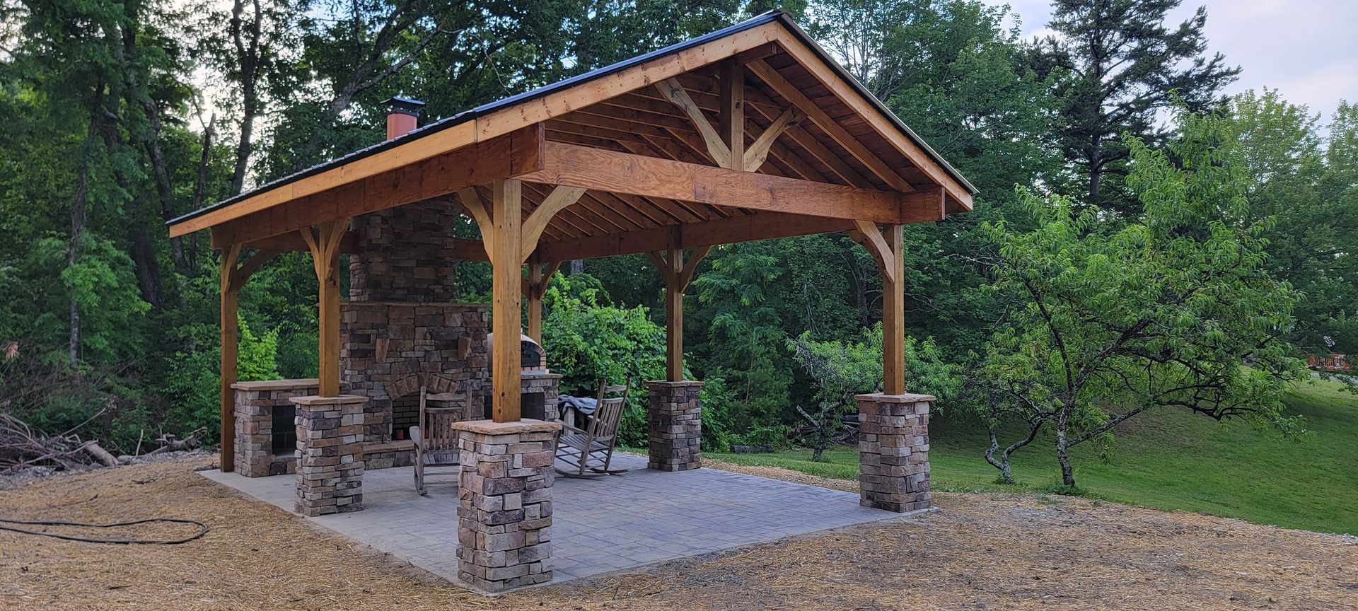 A wooden pavilion with a stone fireplace in the middle of a field.