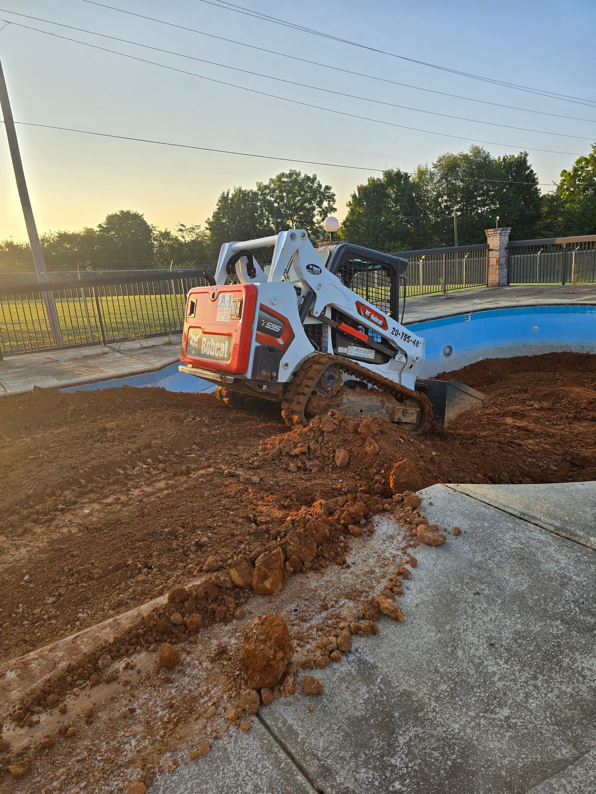 A bulldozer is digging a hole in the ground next to a pool.