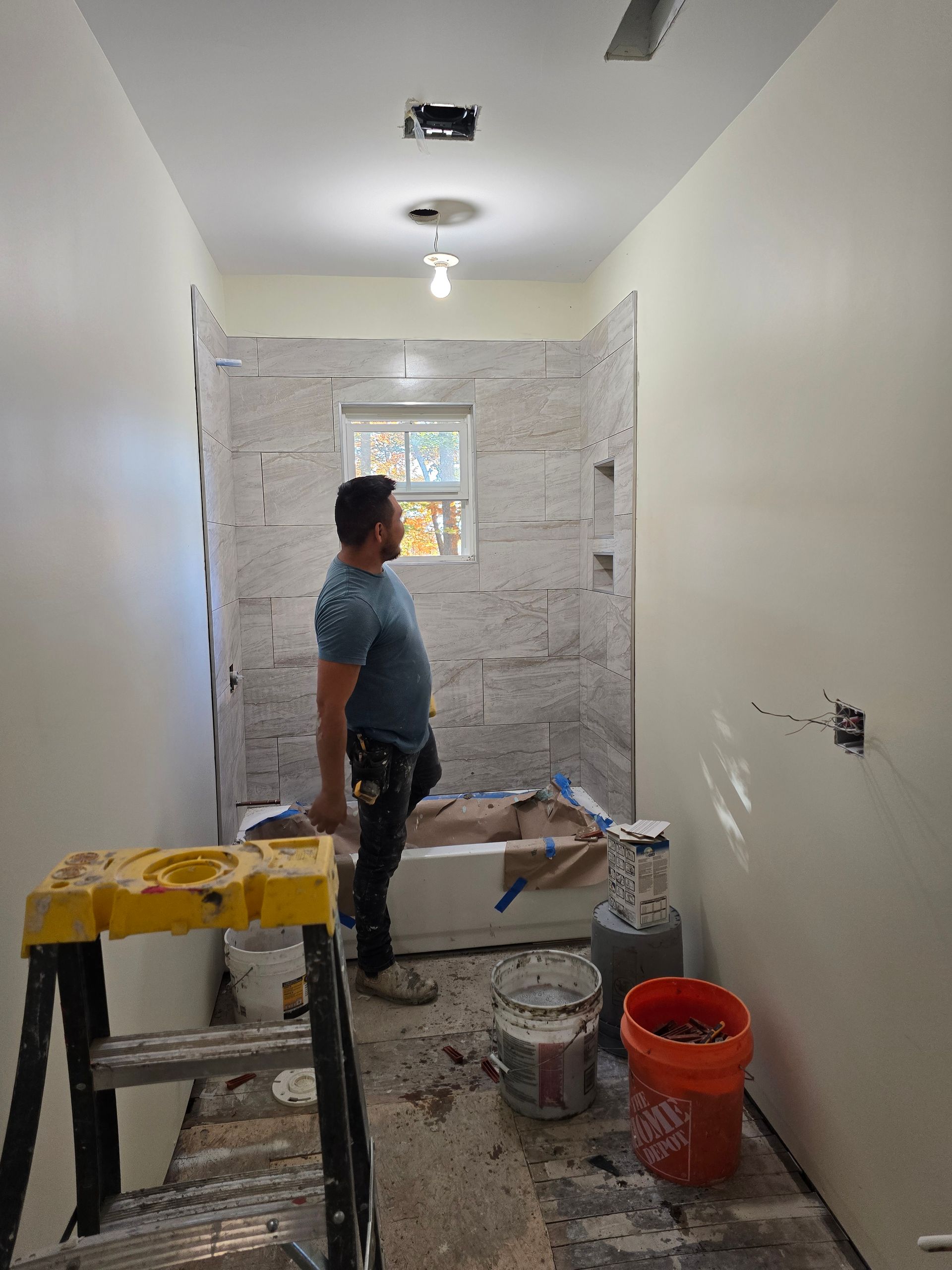 A man is standing next to a bathtub in a bathroom under construction.