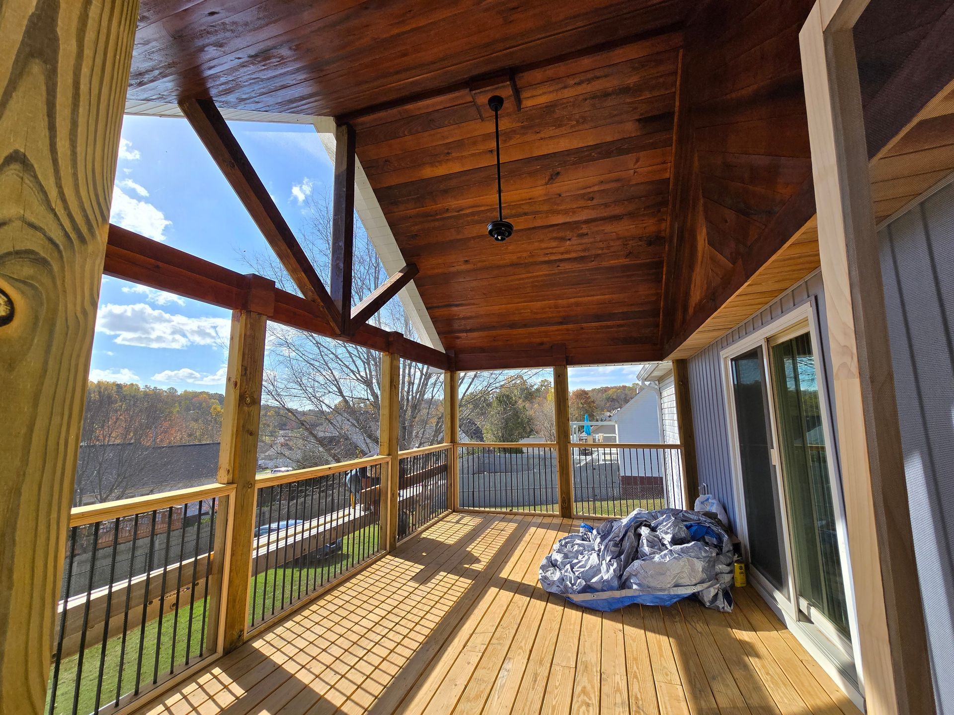 A screened in porch with a wooden deck and a ceiling fan.
