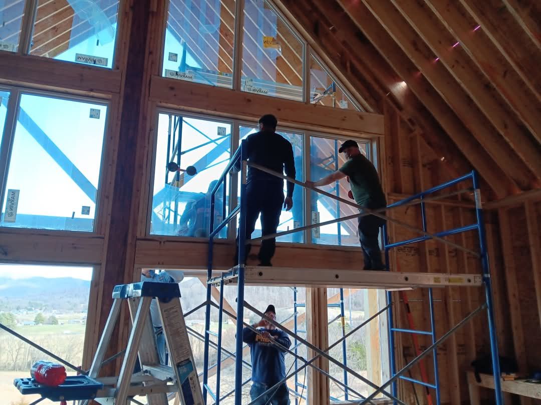 Two men are standing on a scaffolding in front of a large window.