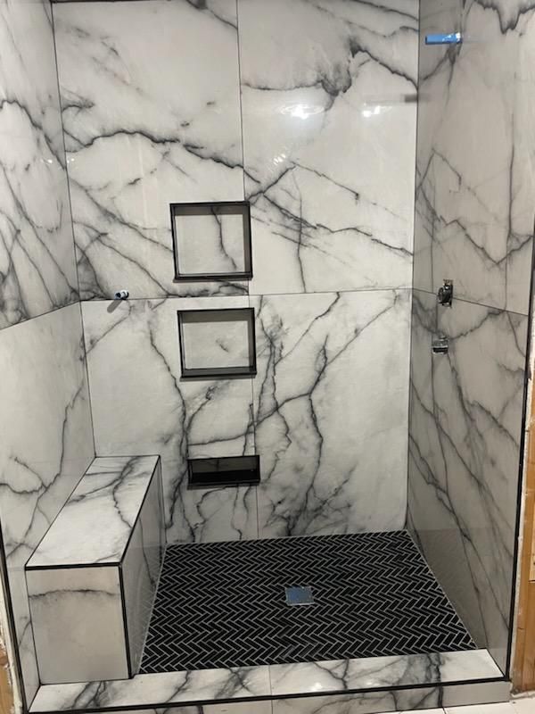 A shower stall with marble walls and a black tile floor.