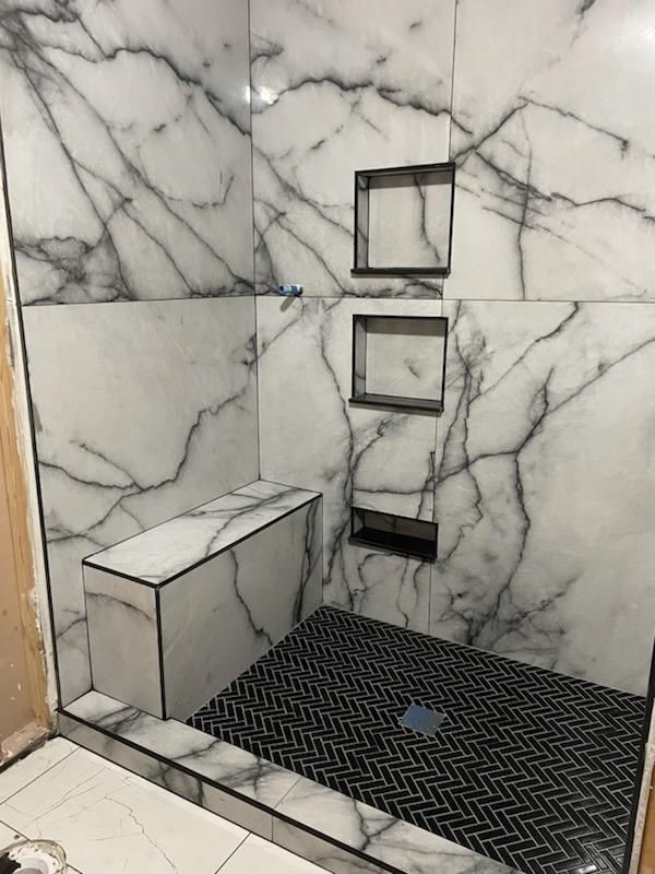 A bathroom with marble walls and a walk in shower with a bench.