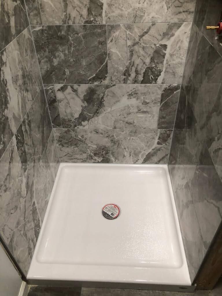 A white shower tray is sitting in a bathroom next to a tiled wall.