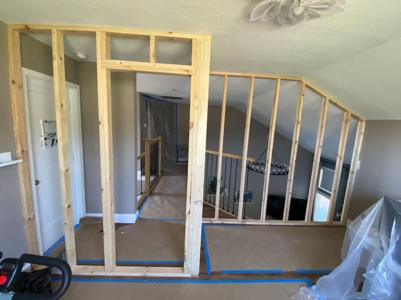 A wooden wall is being built in a room with a staircase.