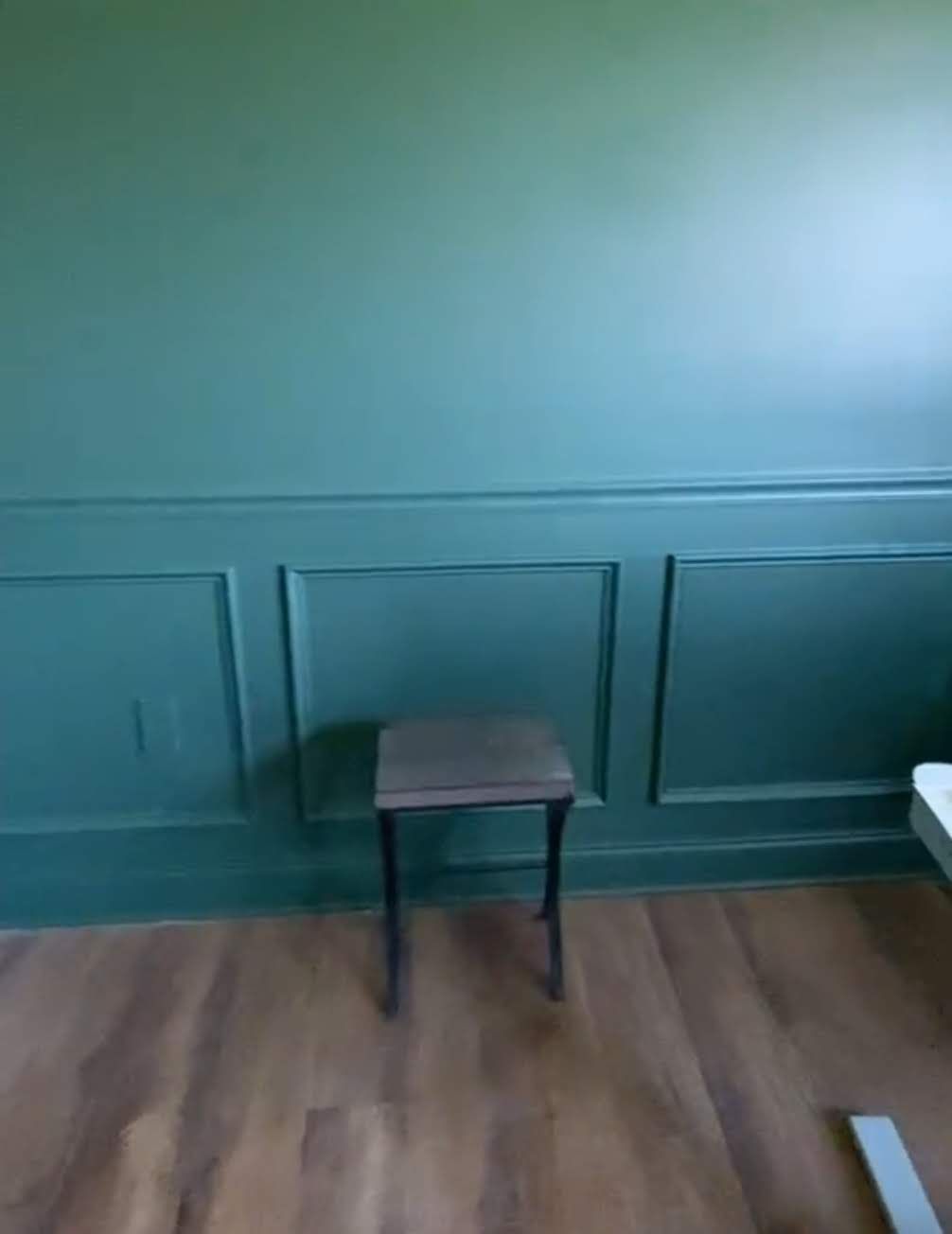 A small wooden stool is sitting in front of a green wall.
