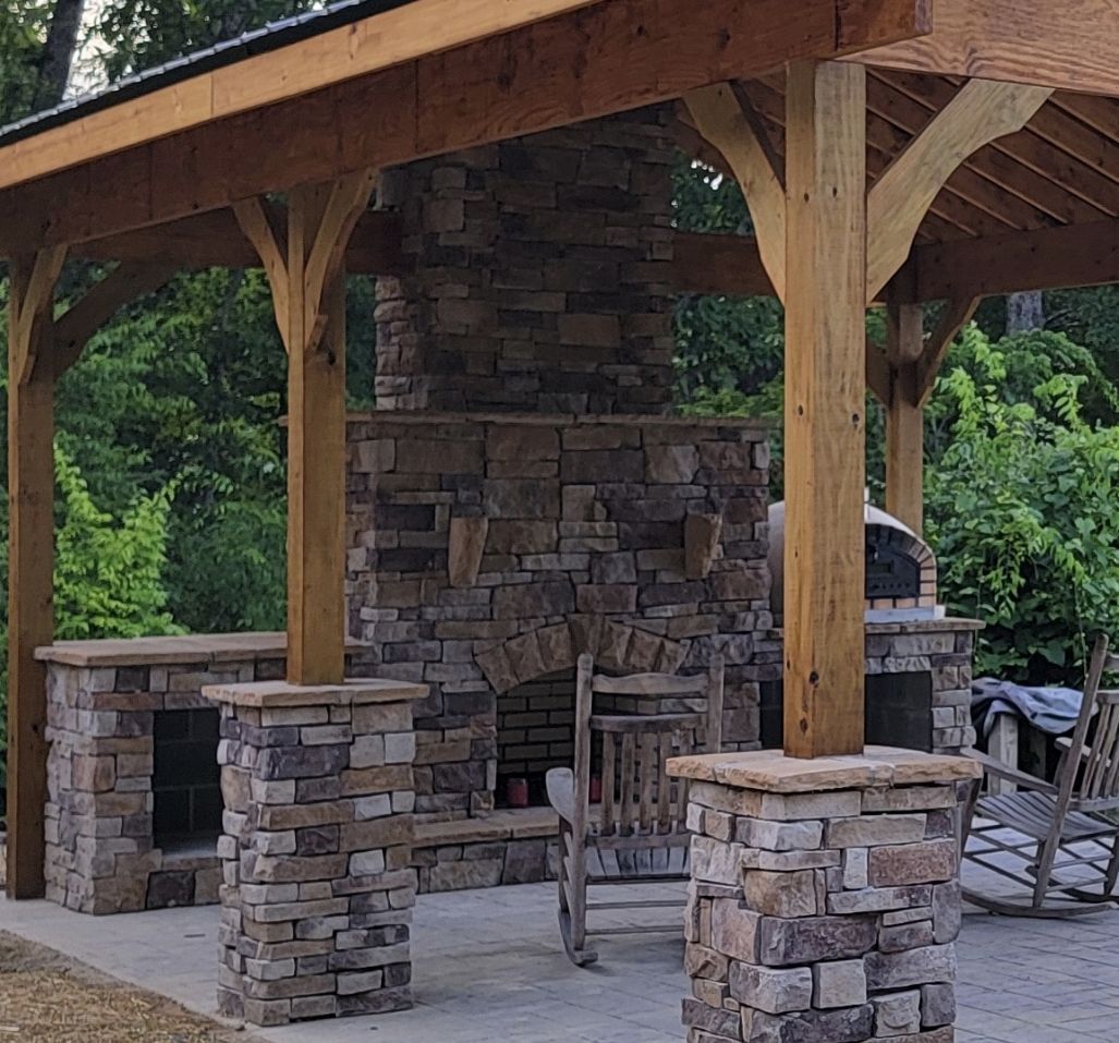 A stone fireplace under a wooden canopy with rocking chairs