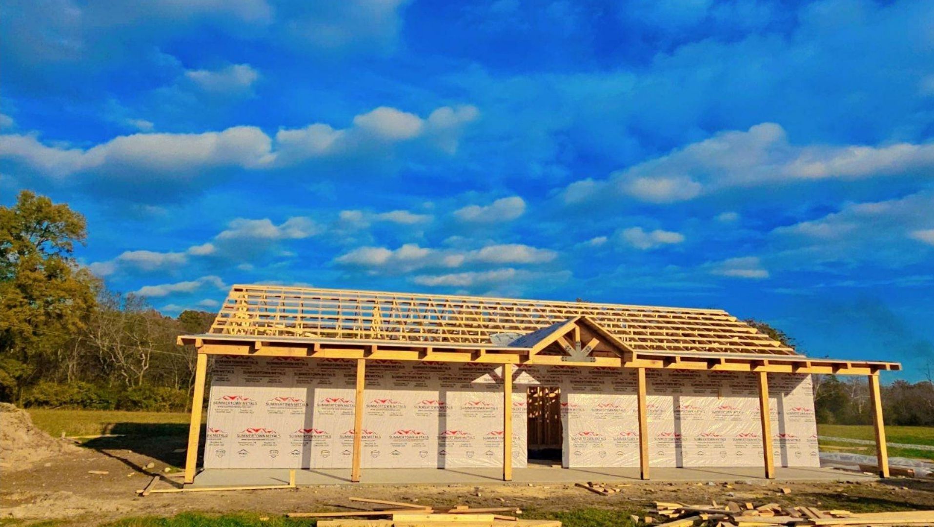 A house is being built in a field with a blue sky in the background.