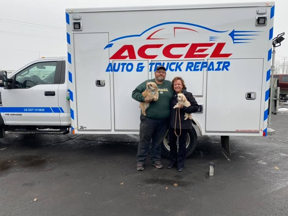 A man and woman are standing in front of a truck that says accel auto & truck repair.