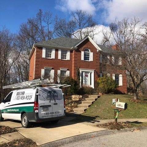Brick house with new roof, van parked in front, ladder on roof.