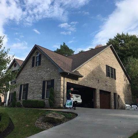 Brick house with attached garage, person loading items into a car parked inside.