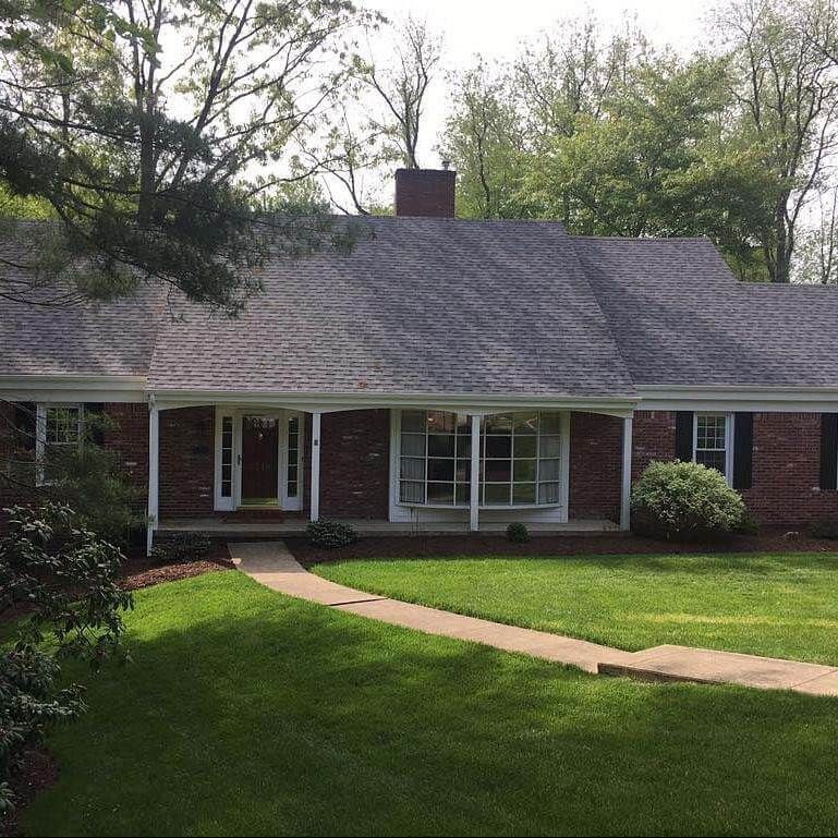 Brick ranch home with green lawn, walkway, and trees.