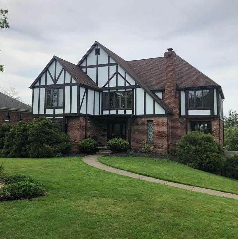 Tudor-style house with brick and dark trim. Green lawn and bushes surround the home.