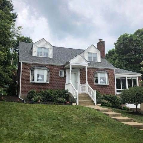 Brick house with white trim, dormers, and a small porch on a green lawn under a cloudy sky.