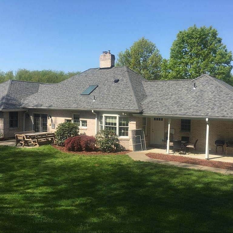 Low-slung house with gray roof, green lawn, trees, and covered porch.