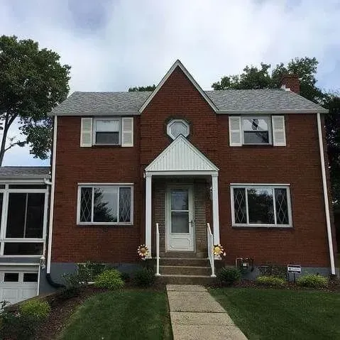 Red brick two-story house with a gabled roof and white trim. A porch and sidewalk lead to the front door.