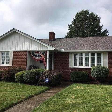 Brick house with white trim, green lawn, bushes, and a patriotic banner.