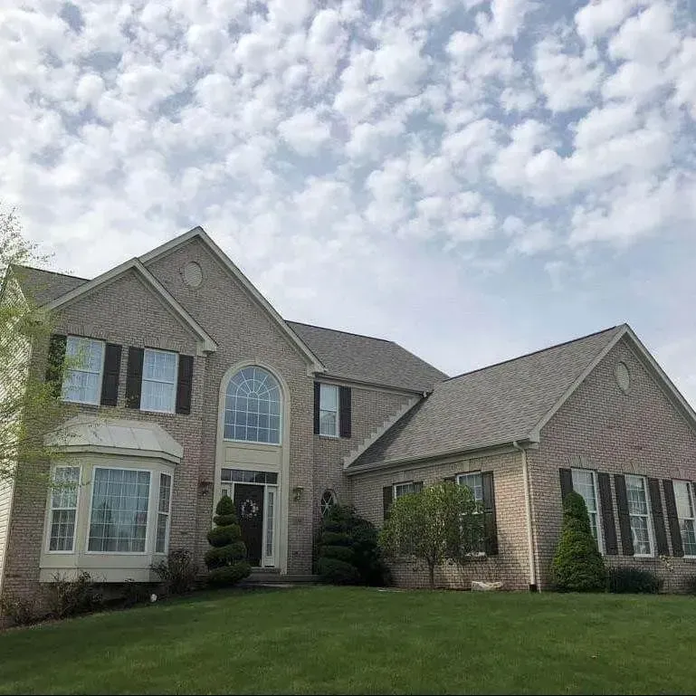 Two-story brick house with dark shutters, a bay window, and a well-manicured lawn under a cloudy sky.