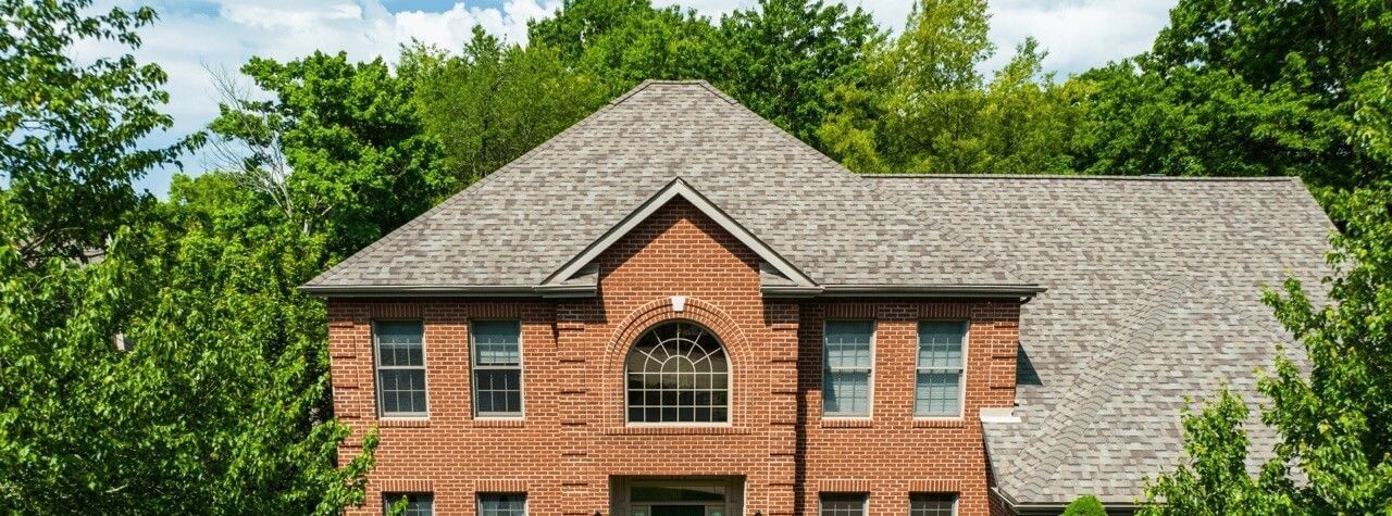 Brick house with a gray roof and surrounded by green trees.