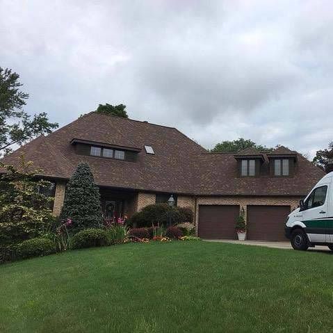 Brick house with brown roof, green lawn, two-car garage, and a white van parked in front.