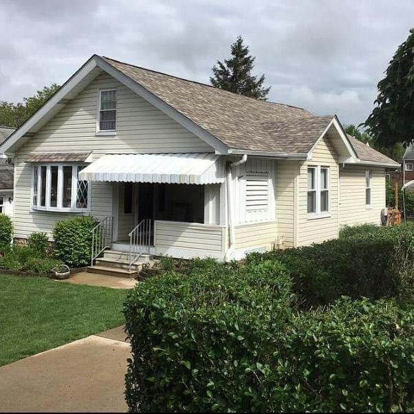 Beige house with a small front porch, covered by an awning. Lush green bushes line the yard.