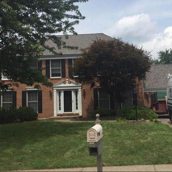 Two-story brick house with black shutters, green lawn, trees, and a mailbox.