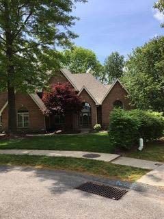 Brick house with tan roof surrounded by trees and green lawn.
