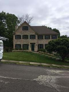 Two-story brick house with green lawn, trees, and cloudy sky.