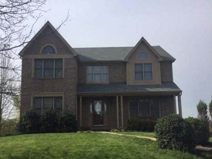 Two-story brick house with a green roof, brown siding, and bushes in front.