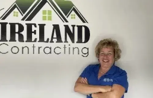 Woman in blue shirt smiling, arms crossed, in front of 