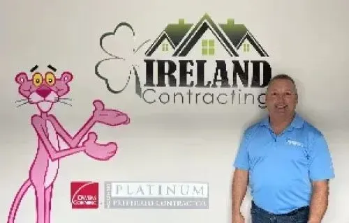 Pink Panther and man stand in front of Ireland Contracting logo. Man wears blue shirt, Pink Panther gestures.