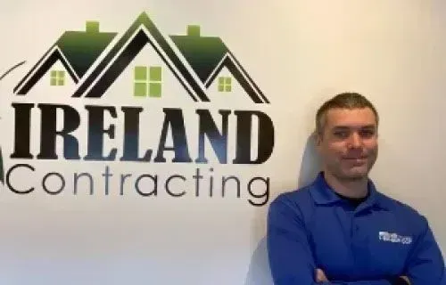 Man in blue shirt with arms crossed, standing in front of 