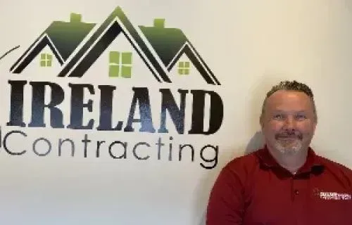 Man in red shirt stands next to a logo for 