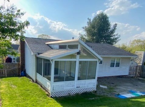 White house with attached screened porch, green lawn, blue sky.