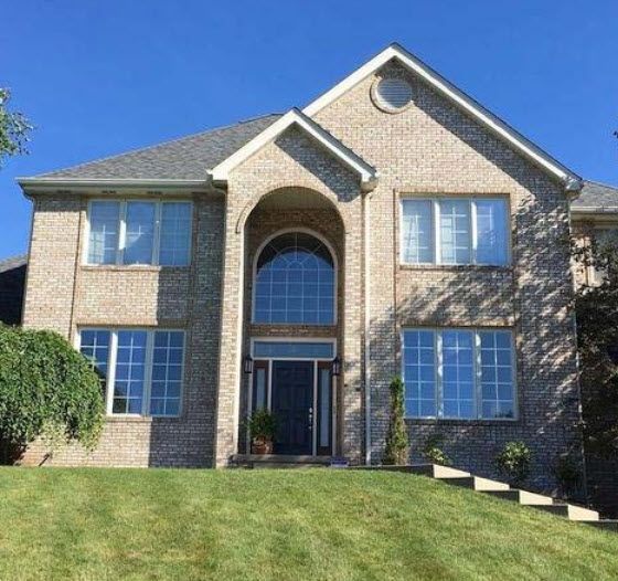Two-story brick house with arched entrance, multiple windows, and a sloped lawn.
