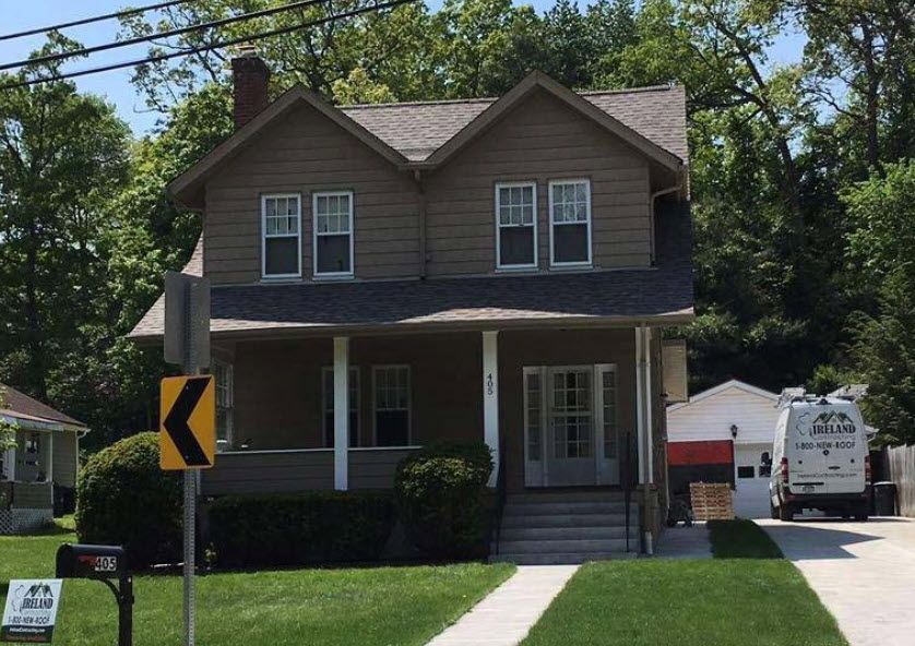 Two-story brown house with a porch and two upper windows. A curved road sign is in the foreground.