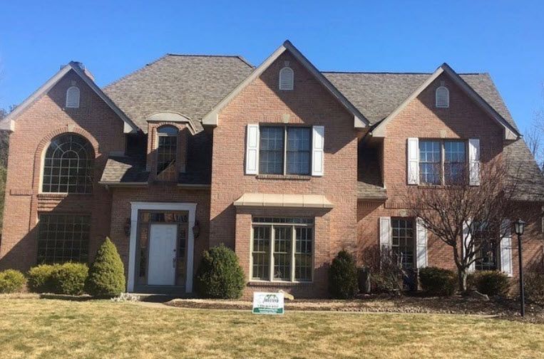 Brick house with multiple gables, white trim, and a brown roof under a clear blue sky.
