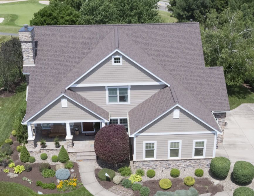Tan two-story house with gray roof, porch, and landscaped yard.
