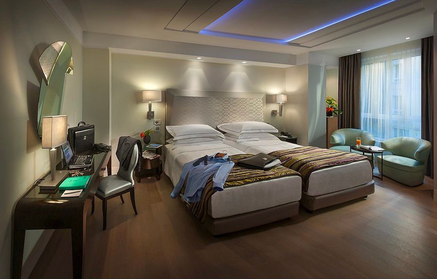 Una moderna camera d'albergo con due letti singoli, una scrivania, una sedia, due poltrone verdi vicino alla finestra.