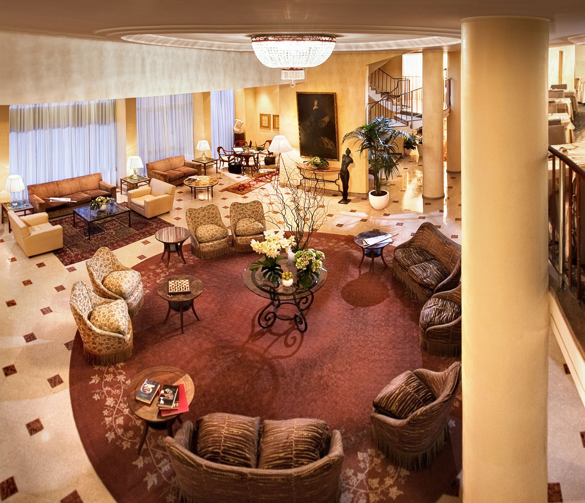 从高角度拍摄的酒店大堂，可以看到一块巨大的圆形地毯、舒适的座椅、温暖的灯光和白色的柱子。