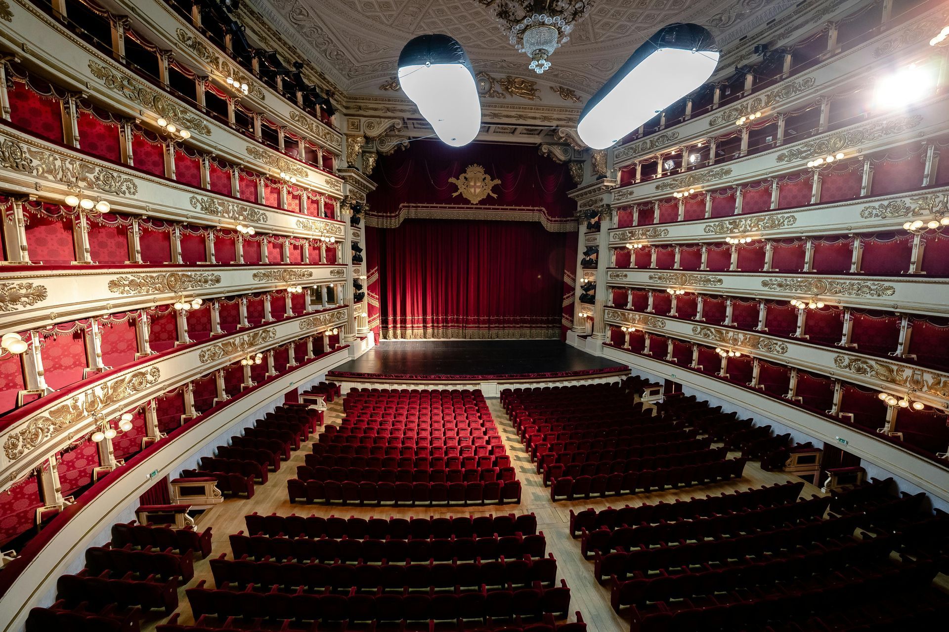 Vista interna di un classico teatro dell'opera a più livelli, con file di poltrone in velluto rosso.